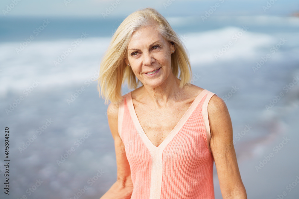 Mature woman enjoying her free time looking at the sea from the shore of the beach.