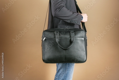 man holds leather briefcase close up, on brown background. Men's leather bag, studio photo shot
