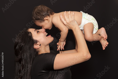 A young mother holds her baby son over her head. Isolated portrait on black background. High quality photo