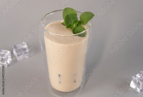 Glass of traditional Indian lassi drink with mango, mint and ice on a grey background.