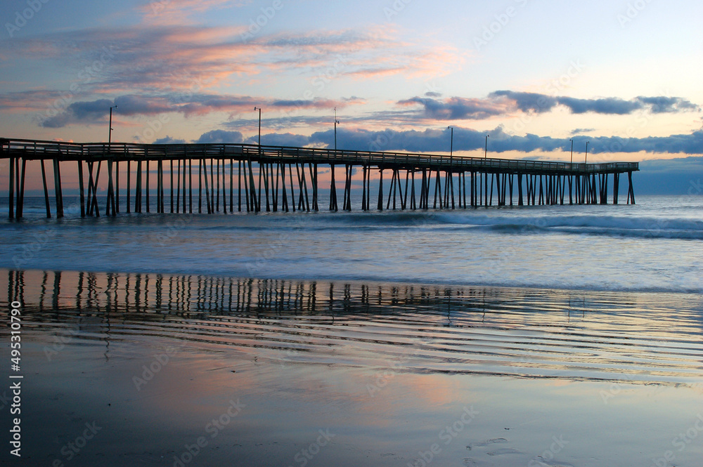 The colorful clouds of sunrise reflect in the waters near the Virginia Beach Fishing Pier