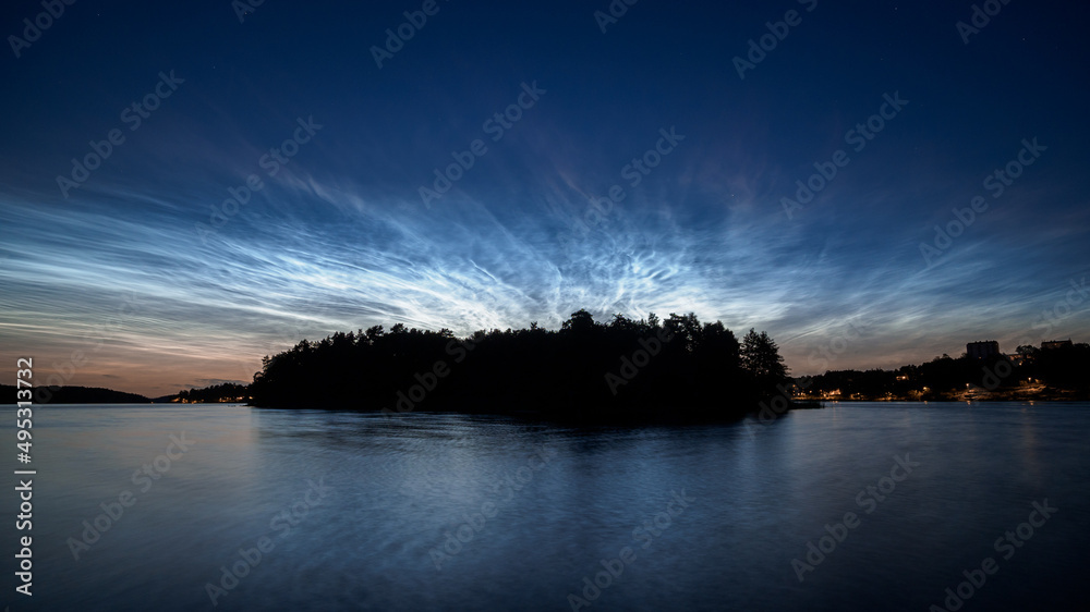 Noctilucent clouds over a tree covered island in a lake