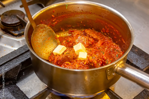 The cook prepares a stew of meat with red hot tomato sauce