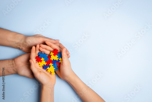 World autism awareness day concept. Adult and child hands holding puzzle heart on light blue background. Top view