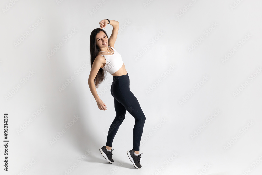 Full length view of smiling young woman posing and jumping on white background. Attractive brunette woman in fashionable sportswear exercising. Healthy lifestyle, sport concept Full length view of smiling young woman posing and jumping on white background. Attractive brunette woman in fashionable sportswear exercising. Healthy lifestyle, sport concept