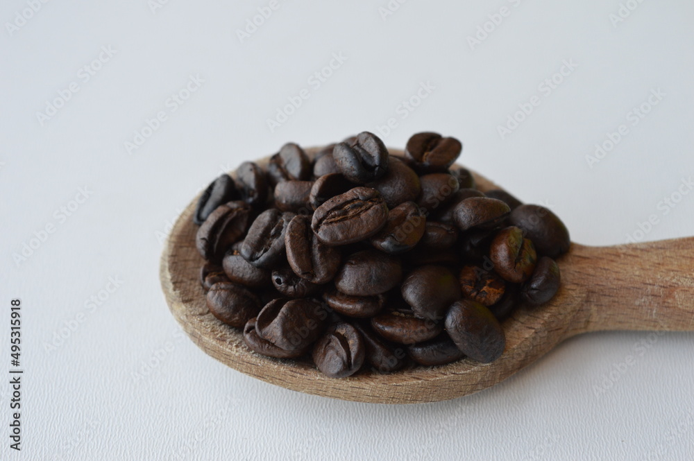 Fototapeta premium Coffee beans in a wooden spoon isolated on white background