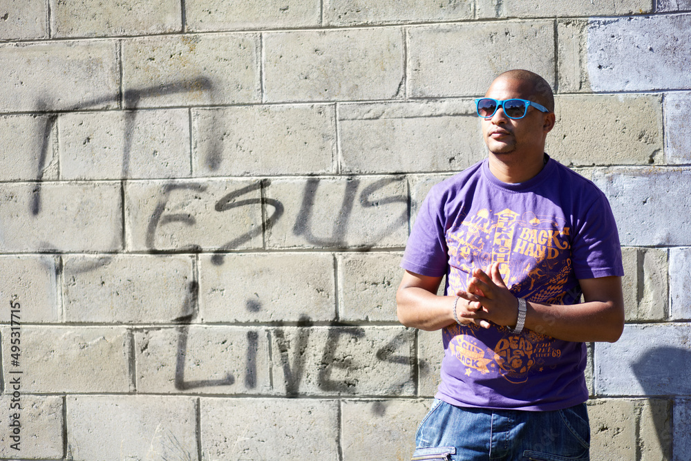 Fototapeta premium Spiritual swag. Shot of a young man standing in front of a wall with graffiti on it.