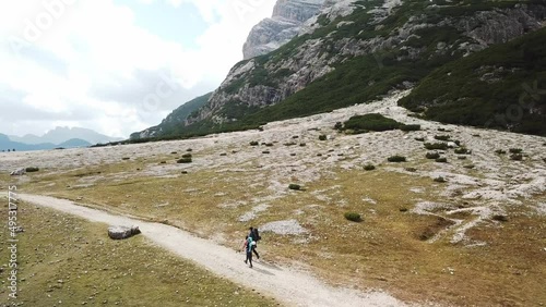 A couple hiking along a gravelled pathway leading through a valley in Italian Dolomites. High, sharp mountains around. Stony and raw landscape. Remote and desolate place. Freedom of exploration
 photo