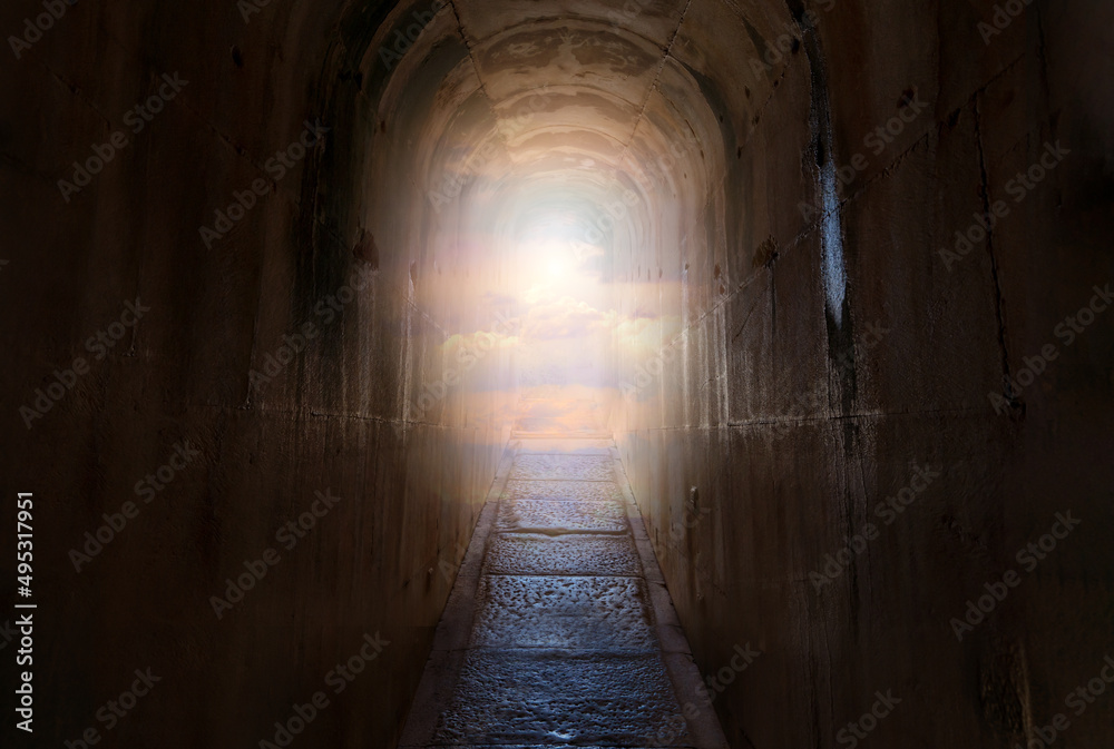 Dark tunnel with narrow path and end of the path shining sky and clouds. Heaven or paradise religion concept.