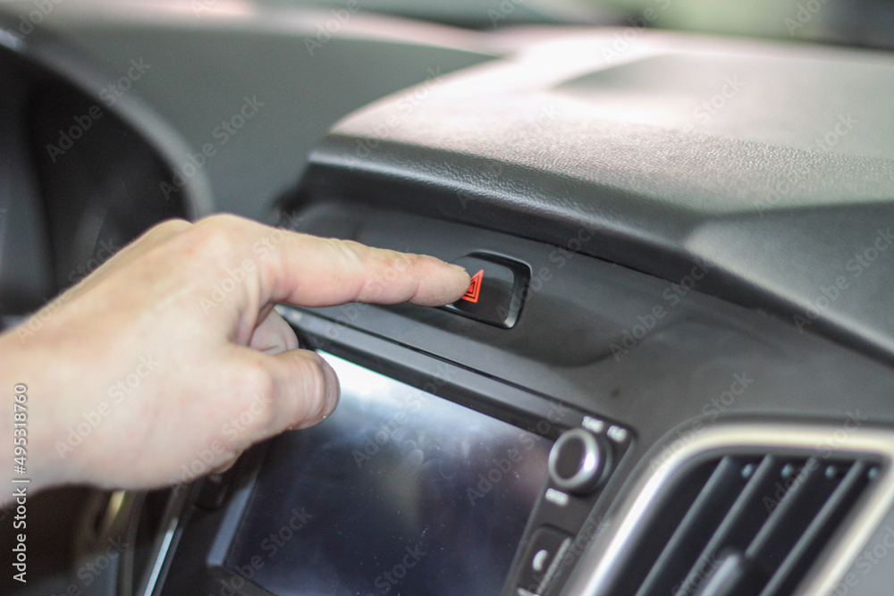 Closeup of man's hand pressing emergency stop button in car. using human hand to push the hazard lights button on the font console controller of the vehicle for emergency situation while driving a car Closeup of man's hand pressing emergency stop button in car. using human hand to push the hazard lights button on the font console controller of the vehicle for emergency situation while driving a car