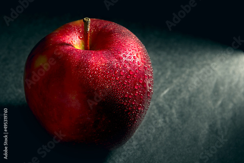Red juicy apple with water droplets on a dark background.