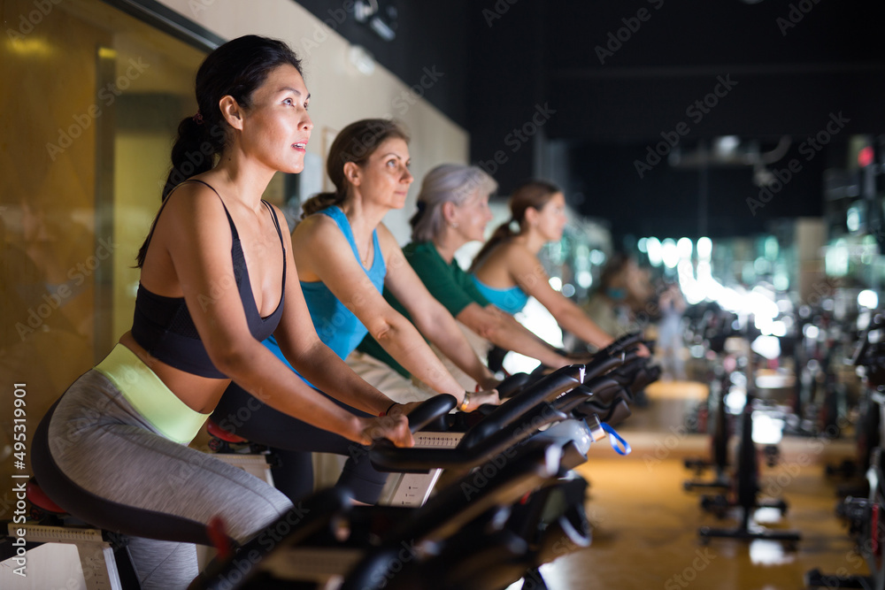 Sporty woman doing cardio workout out in female group, training on exercise bike