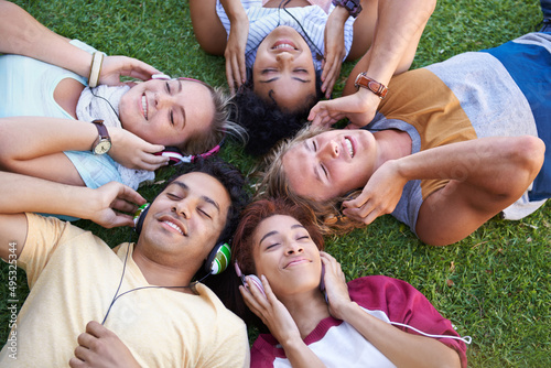 We all love music. High angle of a group of friends lying on their backs on the grass in a park and listening to music.