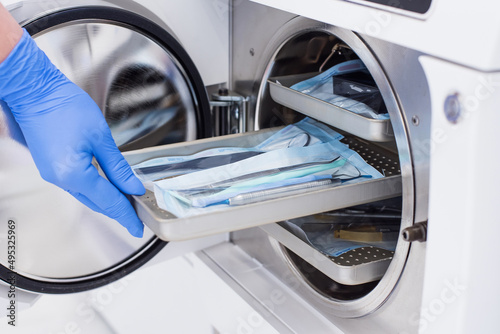 Assistant's hand in gloves insert packaged dental instrument to the autoclave to sterilise.