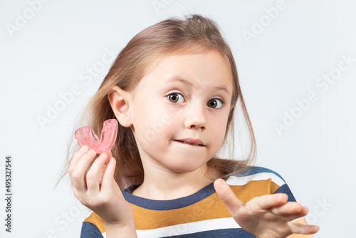 Cute little girl with blond hair is holding a pink dental myofunctional trainer
