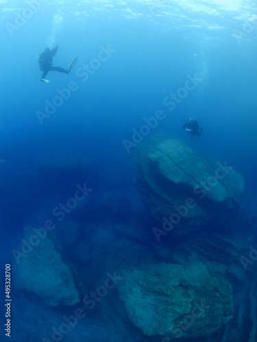 scuba divers around a reef underwater deep blue water big rocks air bubbles rising