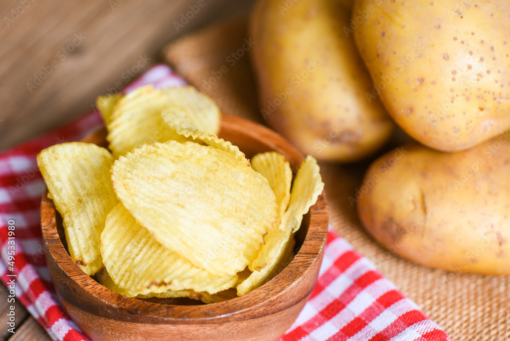 Potato chips snack on bowl, Crispy potato chips on the kitchen table and fresh raw potatoes on wooden background