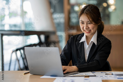 Happy Asian businesswoman laughing sitting at the work desk with laptop, a cheerful smiling female employee having fun feeling joy and positive emotion express sincere laughter at office workplace
