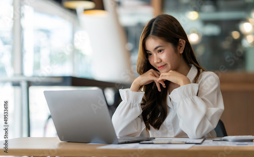 Happy young asian business woman waving hands to greeting partner during making video conference with her team.