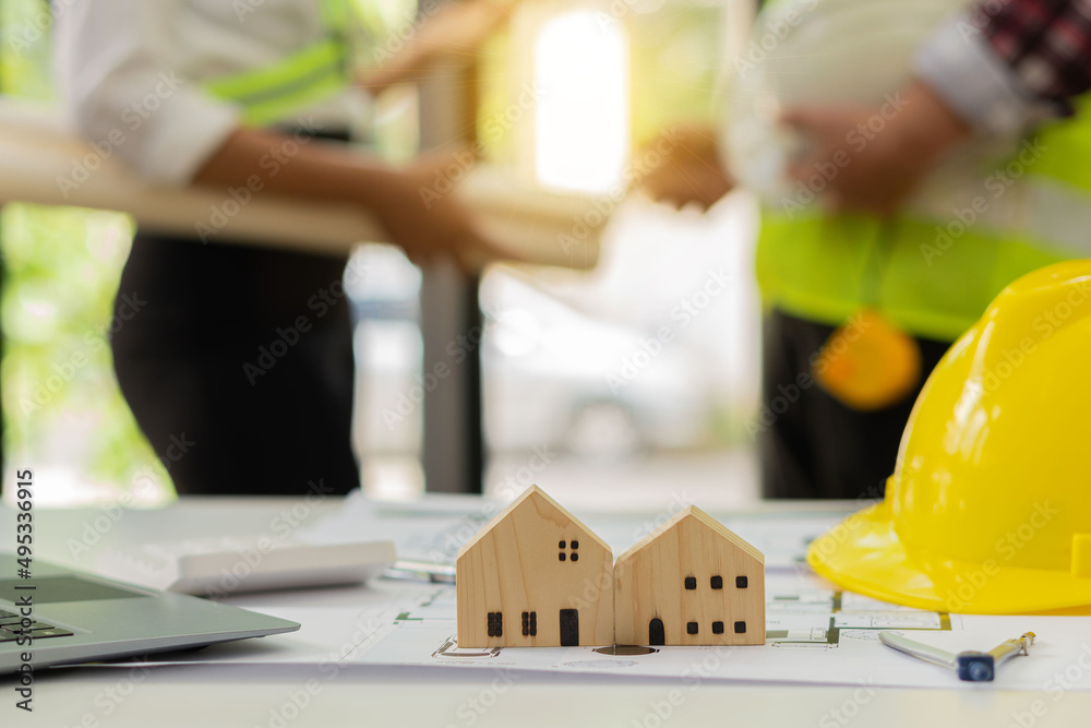 A team of young engineers and architects work, meet, discuss, design, plan, measure the layout of blueprints with tabletop tools in construction concepts with hats and tool houses in front. A team of young engineers and architects work, meet, discuss, design, plan, measure the layout of blueprints with tabletop tools in construction concepts with hats and tool houses in front.