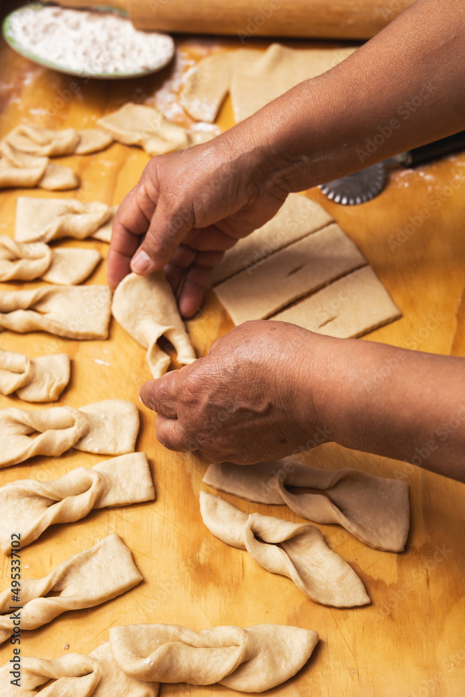 Latin woman's hands kneading dough and making calzones rotos on a wooden table. Chilean fried pastries. Latin food.