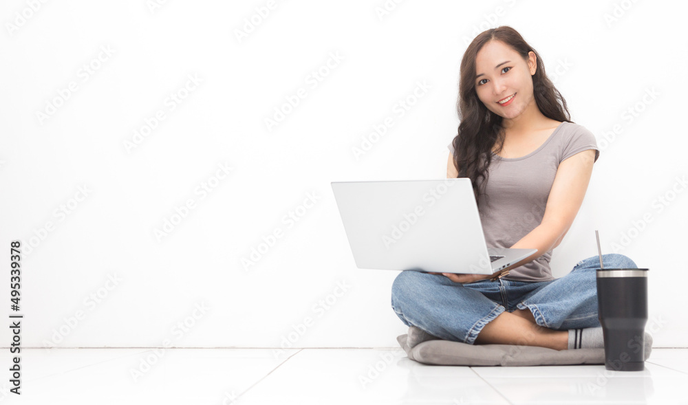 Beautiful Asian woman wearing grey casual shirt using laptop on white background and copy space. Cute Asian woman sitting on the floor room relaxing for work from home concept Beautiful Asian woman wearing grey casual shirt using laptop on white background and copy space. Cute Asian woman sitting on the floor room relaxing for work from home concept