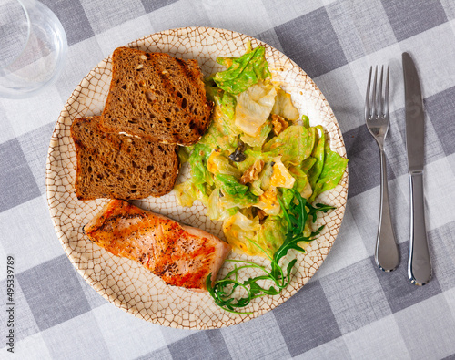 Appetizing baked salmon steak with spices with delicious vegetable salad, served with bread