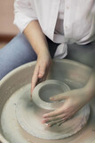 A woman with red hair, white shirt and jeans, in a pottery workshop, working behind a potter's wheel