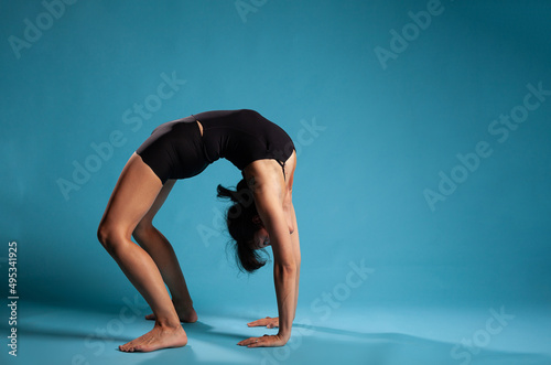 Athletic active person standing in bridge position training body endurance working at healthy lifestyle in studio with blue background. Personal trainer exercising posture