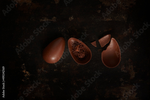 Broken and whole chocolate egg on raw table, top view photo