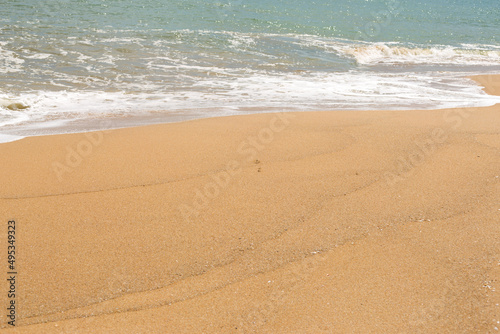 Blue sea waves with foam on yellow sand beach.