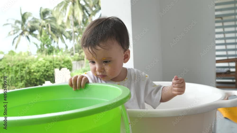 A beautiful baby washes in a white basin in the backyard of his house. Toddler hygiene and daily bathing to improve baby's health. The child cognizes the world and learns to cognize this world. A beautiful baby washes in a white basin in the backyard of his house. Toddler hygiene and daily bathing to improve baby's health. The child cognizes the world and learns to cognize this world.