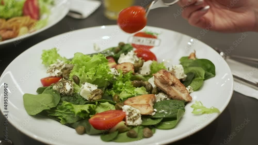 Plate Of Appetizing Salad With Shrimp Tomatoes Cheese And Lettuce. Woman Stabs Half Tomato On Fork. Plate Of Appetizing Salad With Shrimp Tomatoes Cheese And Lettuce. Woman Stabs Half Tomato On Fork.