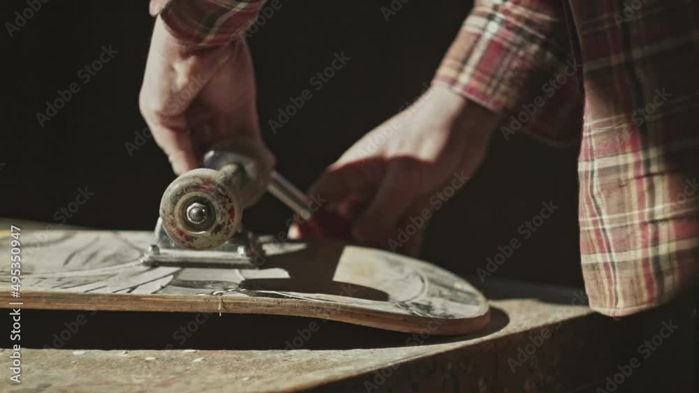 Close-up skateboard, Male person doing maintenance on a skateboard in his workshop with Allen key or Hex key tool. Maintenance of professional skateboarding Close-up skateboard, Male person doing maintenance on a skateboard in his workshop with Allen key or Hex key tool. Maintenance of professional skateboarding
