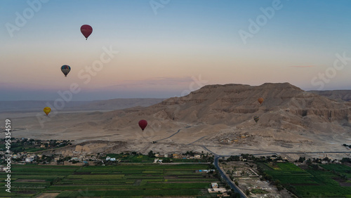 Balloons are flying in the pinkish-blue morning sky over Luxor. Below you can see cultivated fields, a sandy archaeological zone, a picturesque mountain. Egypt