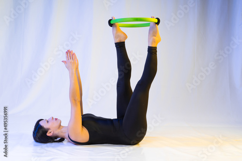 athletic woman doing pilates toning exercises for abs with a circle, crunches to strengthen the abdomen using a pilates magic circle, wearing sportswear in a yoga studio or at home