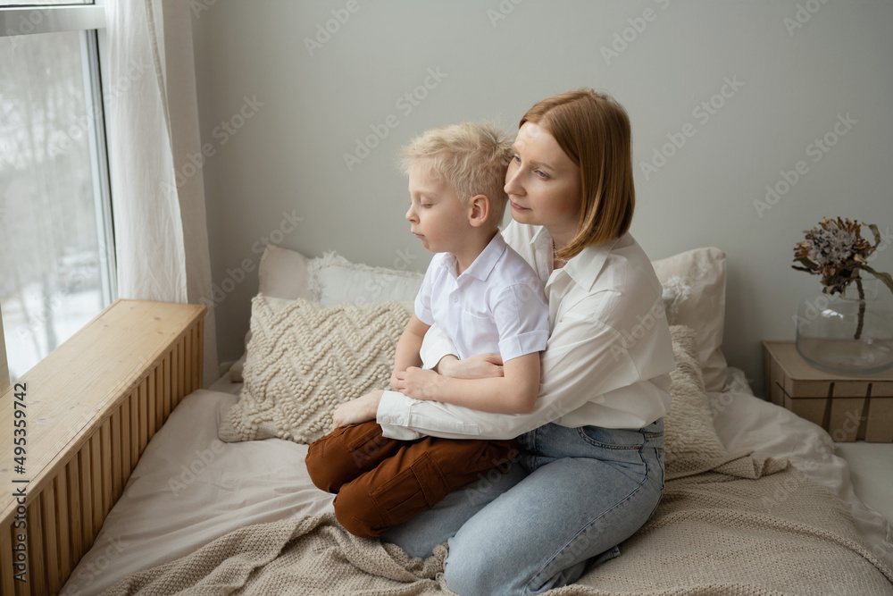 Mom and son with blond hair spend a good time hugging. Portrait of a family in the interior. Mother's Day. The relationship of children and their parents. Mom and son with blond hair spend a good time hugging. Portrait of a family in the interior. Mother's Day. The relationship of children and their parents.