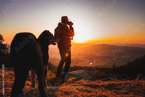 Photographer with camera and dog in sunset taking photos of landscape. Travel Lifestyle hobby concept adventure active vacations outdoor