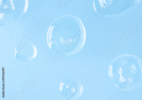 Several transparent drops of hyaluronic acid on a blue background  top view. Skin care and moisturizer.