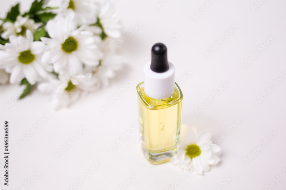 Top view on a glass bottle with essential oil and a chamomile flowers. White background. The concept of organic natural cosmetics Top view on a glass bottle with essential oil and a chamomile flowers. White background. The concept of organic natural cosmetics