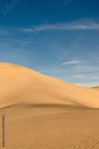 Deserted landscape. Sand dune with dark shadow on a background of blue sky.