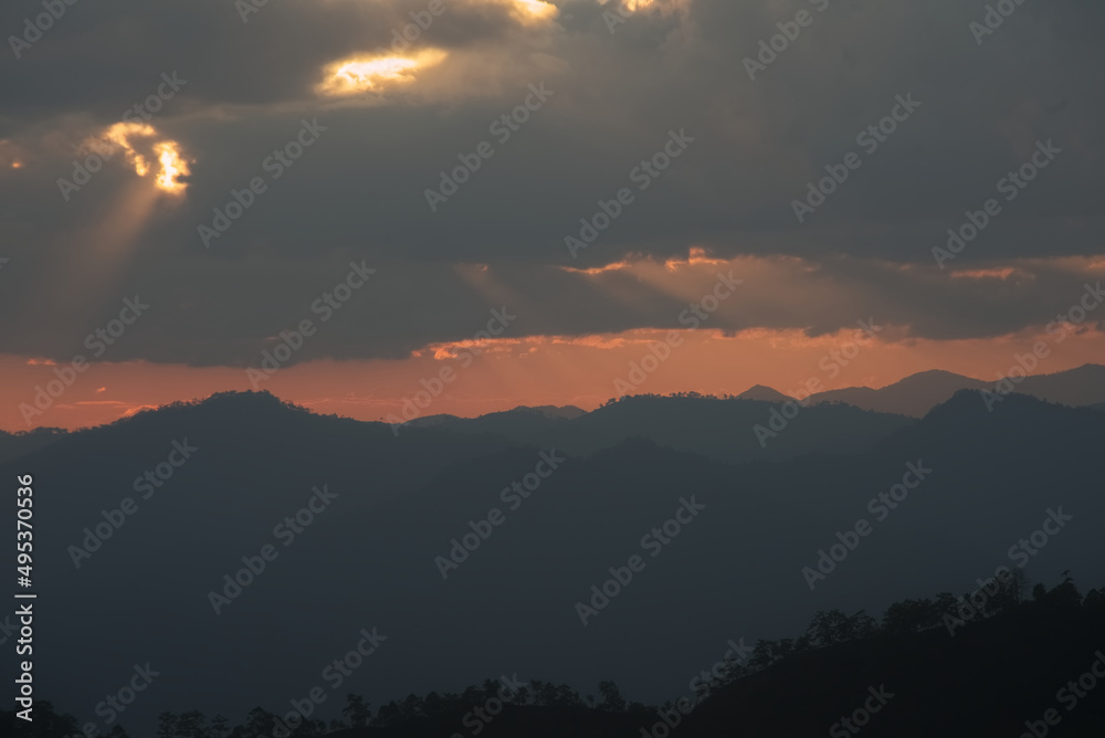 Sun rays over mountain range silhouette in an evening