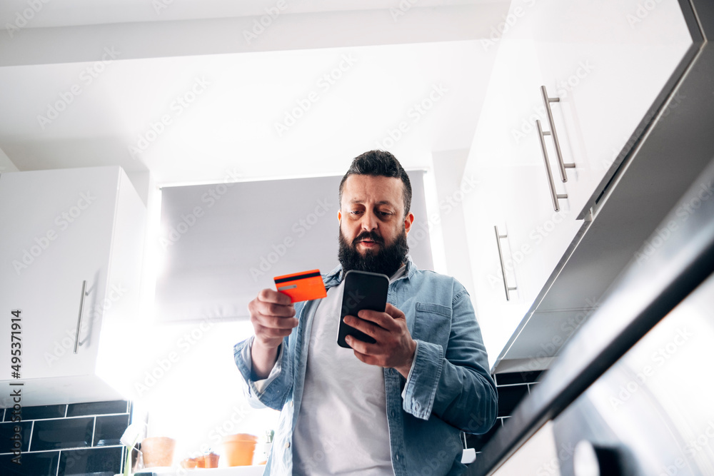 Man with credit card paying financial bill through mobile phone at home Man with credit card paying financial bill through mobile phone at home