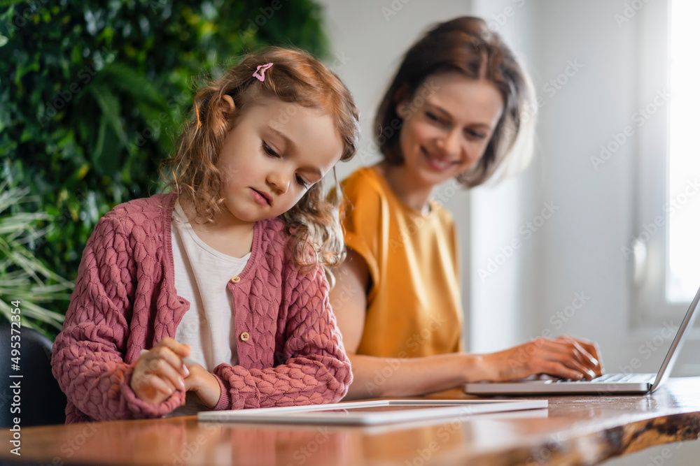 Daughter using tablet PC by smiling mother working at home office Daughter using tablet PC by smiling mother working at home office