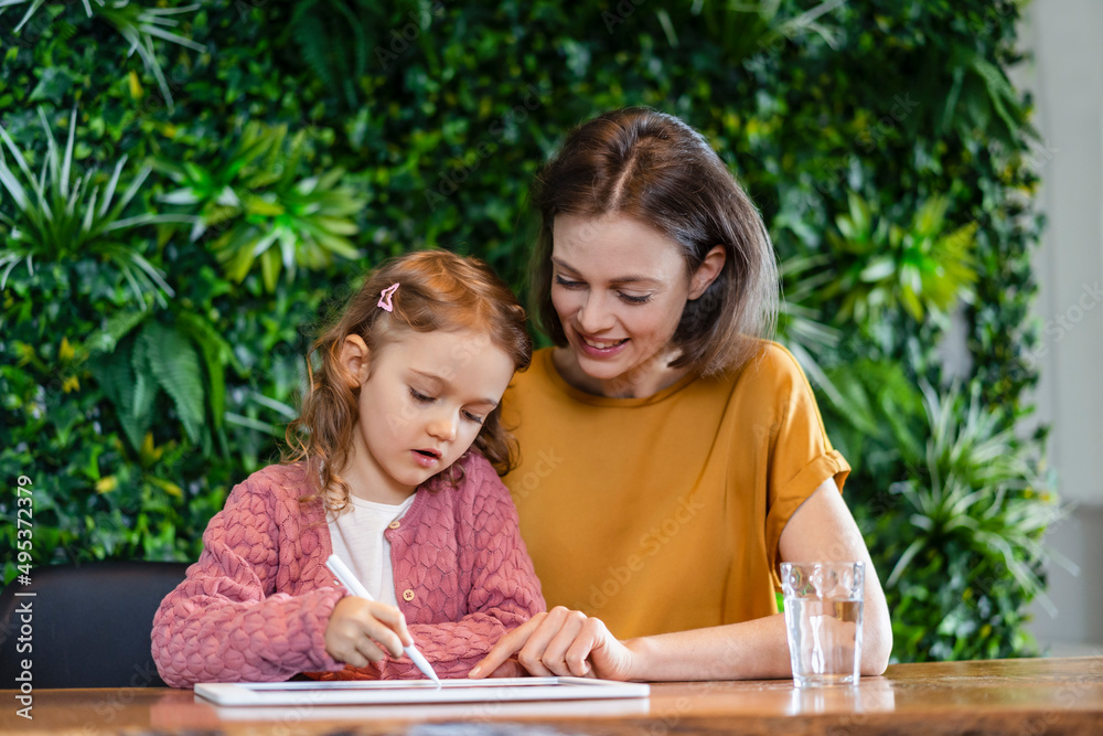Smiling mother helping daughter using tablet PC at home Smiling mother helping daughter using tablet PC at home