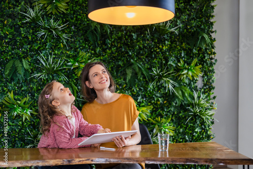 Smiling mother with daughter turning on pendant light with tablet PC at home