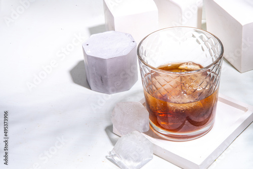 Strong alcohol drink glass. One glass of cognac or whiskey with ice cubes on white tile background with summer sunlight copy space