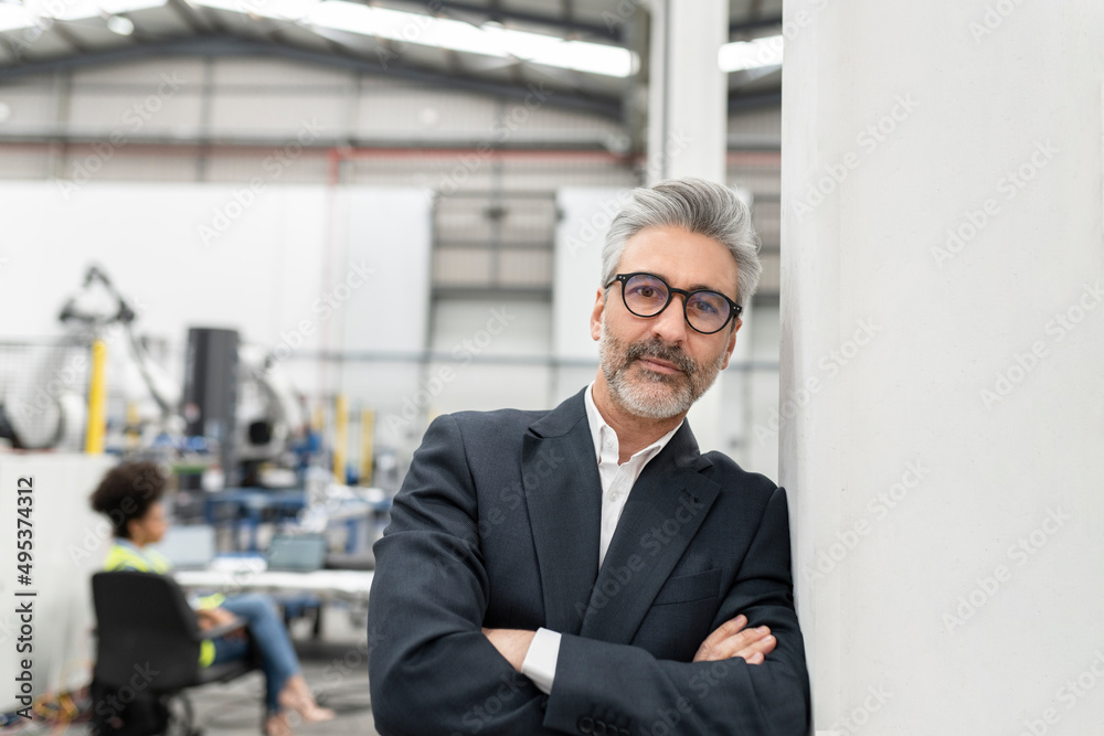 Businessman standing with arms crossed leaning on wall in factory Businessman standing with arms crossed leaning on wall in factory