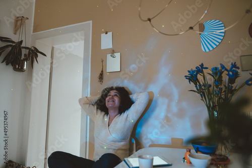 Smiling woman with hands behind head looking at astro light effects in room