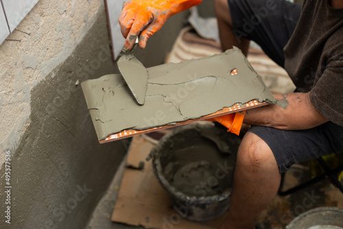 Builder tiling a concrete wall with decorative ornamental tiles lining up a tile with his gloved hands to seat into the tiling cement on the wall.